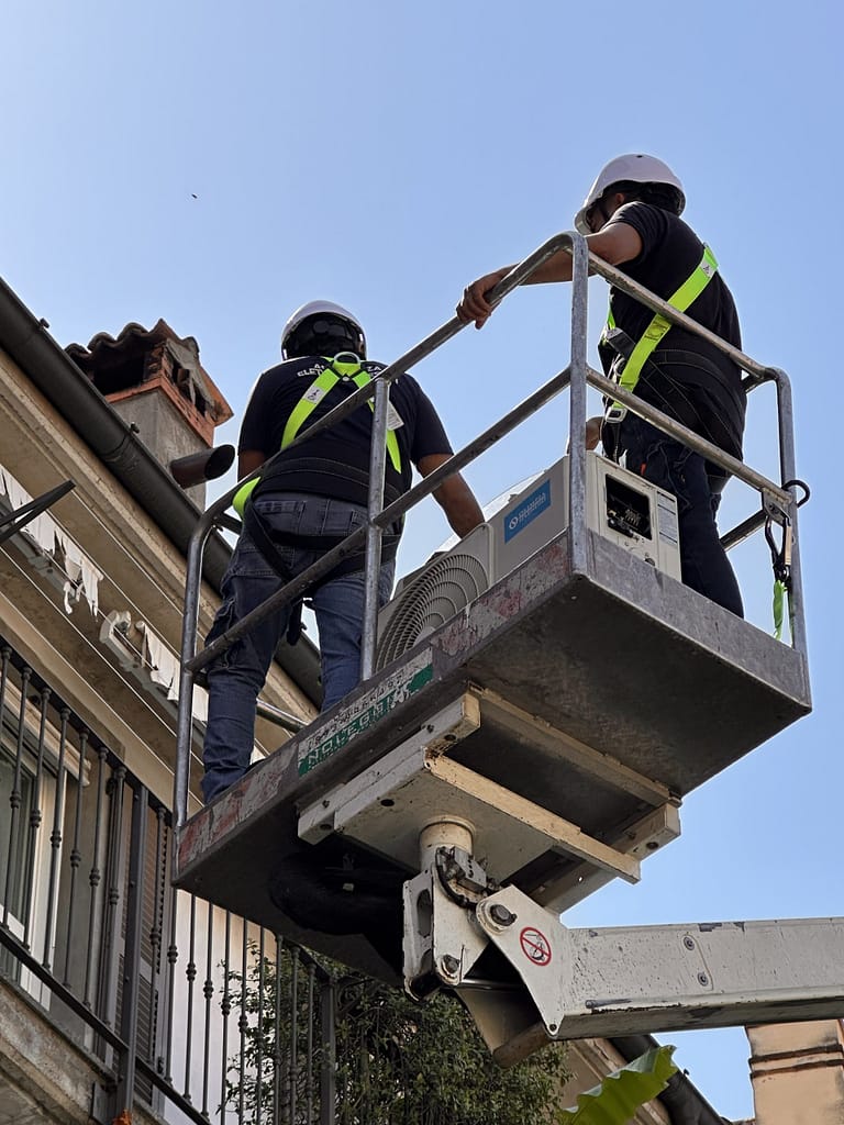 Due tecnici DanorAssistance su piattaforma aerea con imbracatura e caschetto per la sostituzione urgente di un condizionatore a Milano.